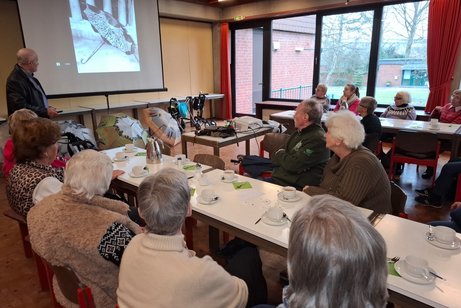 Ein Mann steht vor einer Leinwand und h&auml;lt einen Vortrag vor einer Gruppe.