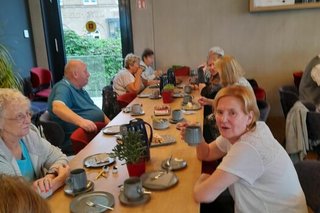 Menschen sitzen gemeinsam beim Essen an einem langen Holztisch.