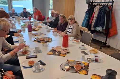 Menschengruppe am Tisch zum Fr&uuml;hst&uuml;ckstreff