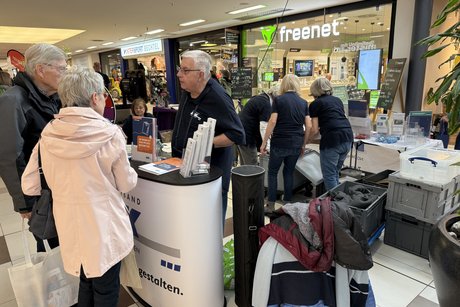 Ein Mann informiert zwei Personen vor dem Info-Stand.