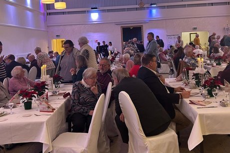 Ein Saal voller Menschen, die an weihnachtlich eingedeckten Tischen sitzen.