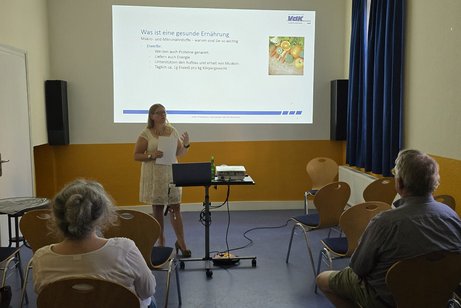 Menschen auf Stühle die der Vortragenden im Vordergrund lauschen