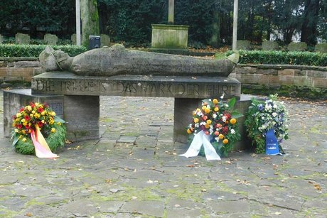 Bild der Kränze am Denkmal: ein aufgebahrter Soldat aus Stein mit der Inschrift "Die Treue ist das Mark der Ehre".