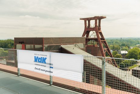 Ein VdK-Banner hängt an einem Geländer vor dem Ausblick auf einen Förderturm