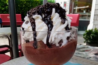 Ein großer Eisbecher aus Glas mit Schokoladeneis, Sahne und Schokosauce steht auf einem Tisch garniert mit einem Schild, auf dem reserviert steht.