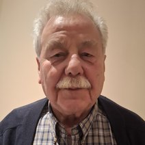 Abgebildet ist Udo Horsthemke. Er trägt ein kariertes Hemd, hat kurze graue Haare und einen Oberlippenbart