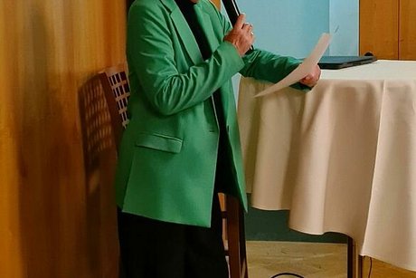 Eine Frau steht mit Mikrofon in der Hand an einem Stehtisch