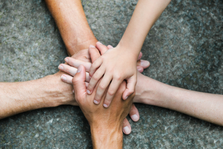 Fünf verschiedene Hände sind sternförmig übereinander gefaltet.