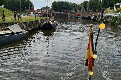 Blick vom Heck eines Schiffs auf einen Kanal und die Reling, an der eine Deutschlandfahne flattert.