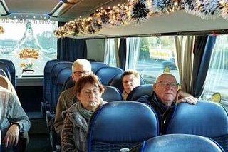 Menschen sitzen in einem Reisebus, dessen Gepäckablage mit Lichterketten und Weihnachtsgirlanden geschmückt ist.