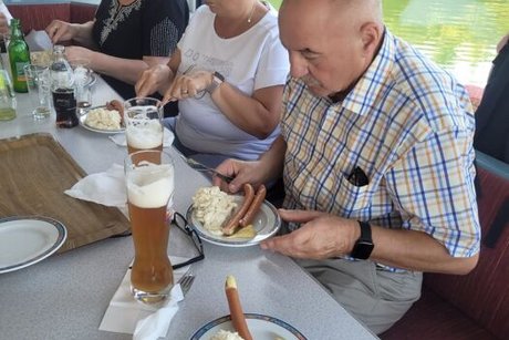 Zwei Frauen und ein Mann sitzen an Deck eines Ausflugsschiffs und genießen dort Bier, Kartoffelsalat und Würstchen.