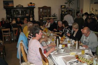 Viele Menschen sitzen gemeinsam beim Frühstück an einem langen Tisch.