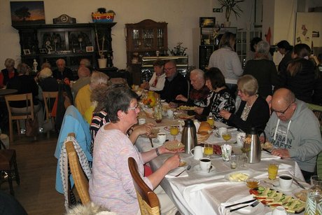 Viele Menschen sitzen gemeinsam beim Frühstück an einem langen Tisch.