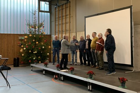 M&auml;nnerchor auf B&uuml;hne stehend mit Weihnachtsbaum im Hintergrund