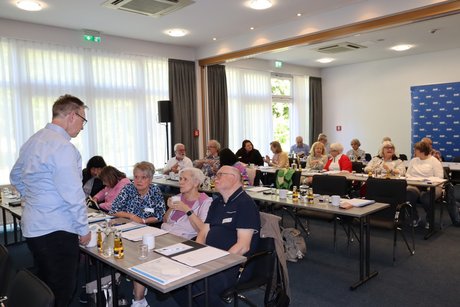 Menschen sitzen an Tischen in einem Saal.