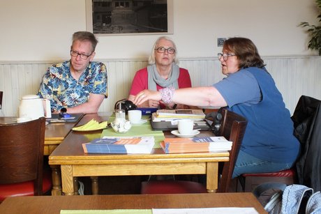3 Personen sitzen am Tisch.