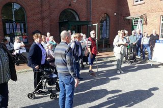 Eine Gruppe Menschen steht auf einem gepflasterten Platz vor dem roten Ziegelbau des Textilmuseums in Bocholt.