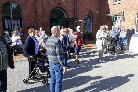 Eine Gruppe Menschen steht auf einem gepflasterten Platz vor dem roten Ziegelbau des Textilmuseums in Bocholt.