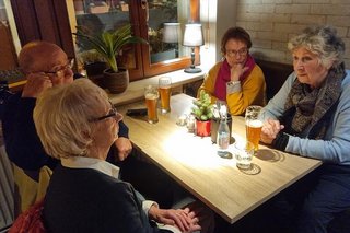 Drei Frauen und ein Mann sitzen bei Bier und Wasser an einem von oben ausgeleuchteten Ecktisch in einer Gaststube.