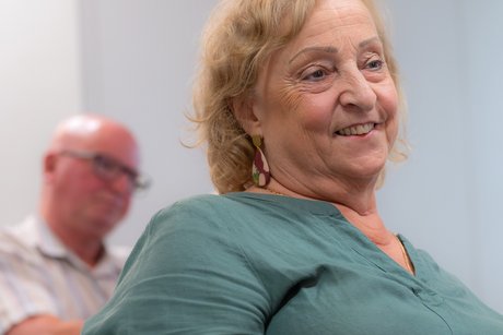 Eine Frau mit mittellangen, leicht gelockten blonden Haaren h&ouml;rt l&auml;chelnd jemandem, der nicht im Bild ist zu.