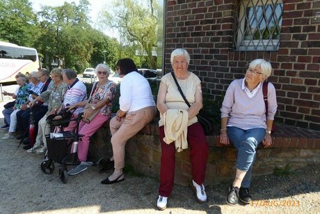 Die Reisegruppe hat auf einem Mäuerchen nebeneinander Platz genommen.
