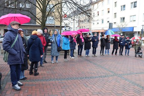 Viele Menschen stehen mit bunten Schirmen nebeneinander.