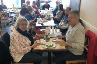 Männer und Frauen sitzen gemeinsam an einer langen Osterfrühstücks-Tafel im Stadtcafé