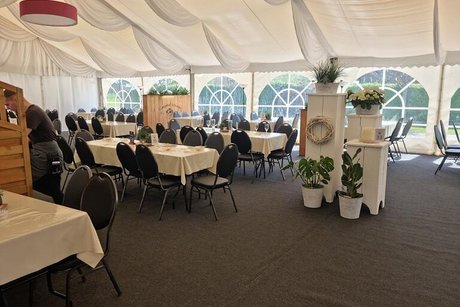 Ein weißes Festzelt ist ebenfalls bestuhlt und mit weißen langen Tischen bestückt und zusätzlich mit Blumenarrangements dekoriert.