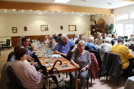 Mitglieder sitzen an langen Tischen und h&ouml;ren dem Vorsitzenden zu.