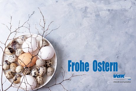 Eine Schale mit naturfarbenen kleinen und gro&szlig;en Eiern und Zweigen auf betongrauem Grund. In blauer Schrift daneben: Frohe Ostern und das Logo des VdK NRW.