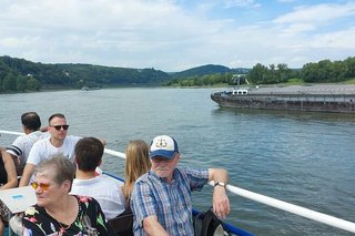 Menschen sitzen am Außendeck eines Ausflugsschiffes, im Hintergrund fährt ein Tankschiff vorbei.