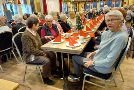 Viele Menschen sitzen an weihnachtlich geschmückten Tischen in einem Saal