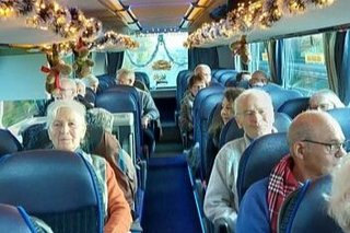 Menschen sitzen in einem Reisebus, dessen Gepäckablage mit Lichterketten und Weihnachtsgirlanden geschmückt ist.