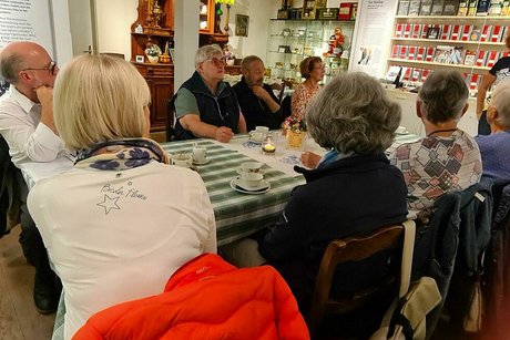 Menschen sitzen an einem Tisch zwischen Ausstellungsstücken des Teemuseums und trinken Tee aus dünnen Porzellantassen.
