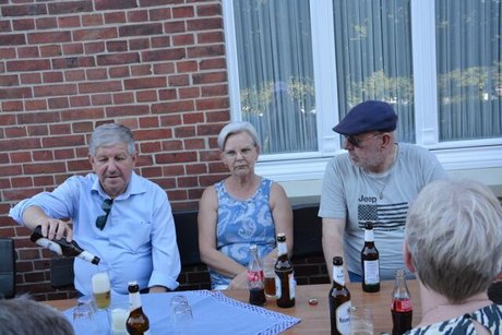 Drei Menschen sitzen nebeneinander an einer Bierzeltgarnitur. Auf dem Tisch Bier und Cola.