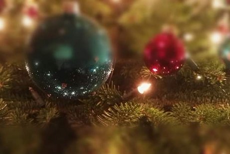 eine grüne und eine rote Weihnachtskugel hängen an Tannen und glitzern.