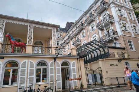 Links im Bild ist das Bürgerbüro mit einer bunten Pferdeplastik auf einem Balkon zu sehen; rechts im Bild sieht man das Rathaus mit geschmiedeten Balkonbrüstungen.