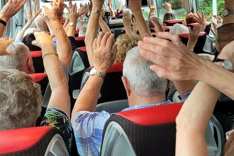 Menschen sitzen im Reisebus und haben die Hänge in die Höhe gestreckt.