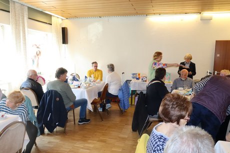 An mehreren gedeckten Tischen sitzen Menschen und unterhalten sich miteinander.