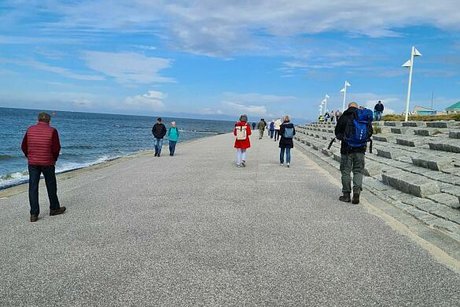 Die asphaltierte Uferpromenade erstreckt sich zwischen Meer und Deichbefestigung bis zum Horizont. Einige Passanten sind zu Fuß dort unterwegs.