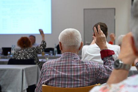 Menschen in einem Saal heben die H&auml;nde zur Abstimmung.