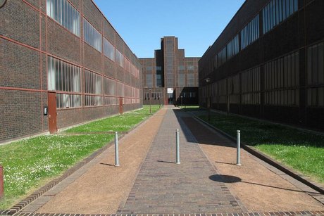 Ein gepflasterter breiter Weg führt zwischen den langgestreckten Zechengebäuden aus roten Ziegelsteinen auf ein weiteres Gebäude zu.