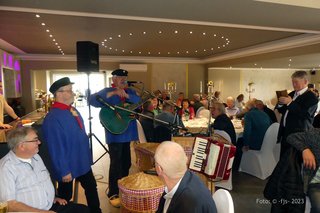 zwei Musikanten und einige Menschen stehen und sitzen im Restaurant