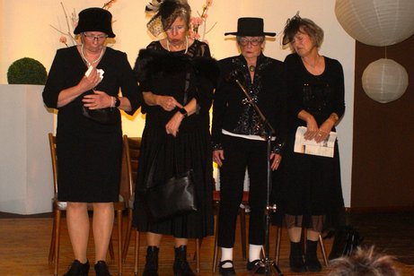 Vier schwarz gekleidete Damen unterhalten sich bei einer Beerdigung.