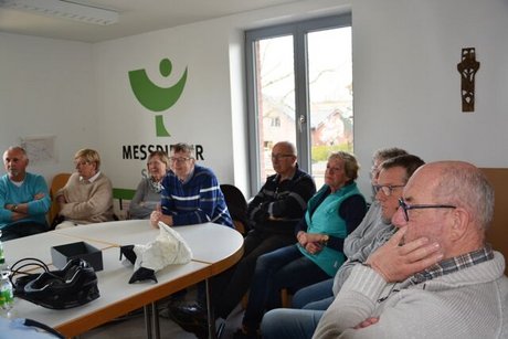 Menschen sitzen um einen Tisch herum. Auf dem Tisch ein Fahrradhelm und ein moderner Fahrradairbag.