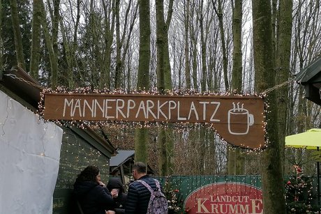 Ein großes Holzschild mit der Aufschrift "Männerparkplatz" bewirbt den Glühweinstand des Weihnachtsmarktes.