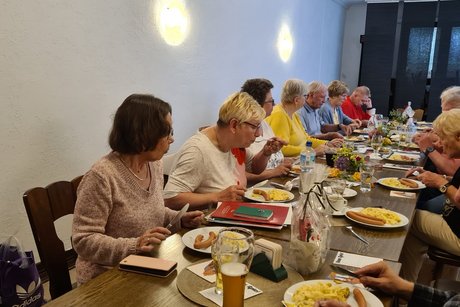 Mitgliedertreffen Mehrere Personen sitzen an einem langen Tisch und speisen gemeinsam.