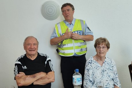 Verkehrsquiz mit Polizeihauptkommissar Hans-Joachim Ruhl. Polizeihauptkommissar Hans-Joachim Ruhl steht zwischen zei sitzenden Mitgliedern.