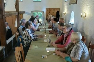 Menschen sitzen in einer Gaststube an einem langen Tisch.