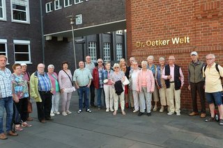 Foto der Reisegruppe vor dem Dr. Oetker Firmensitz unter einem goldenen Schriftzug Dr. Oetker Welt.